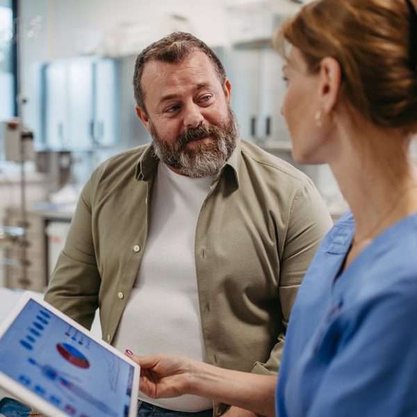 Female doctor consulting with overweight patient, discussing test result in doctor office. Obesity affecting middle-aged men's health. Concept of health risks of overwight and obesity.